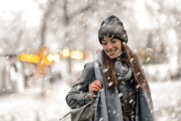 Cheerful smiling woman standing in the snowfall at the park