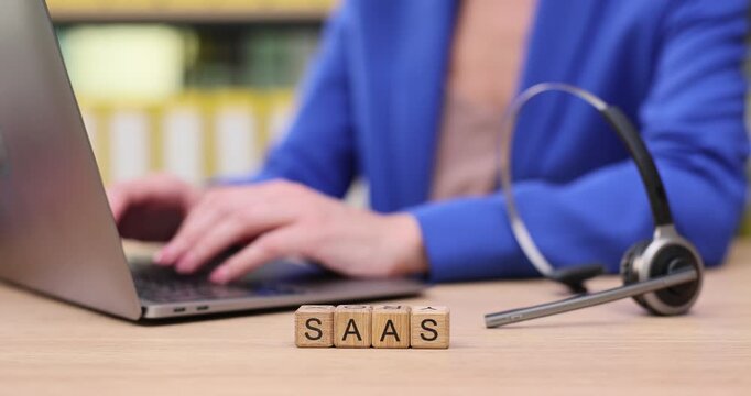 Exploring technology in action as a professional works on a laptop with a headset and blocks spelling SaaS