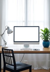 Fototapeta premium Modern home office desk with a blank computer screen, a white lamp, and a green plant by a bright window with sheer curtains.