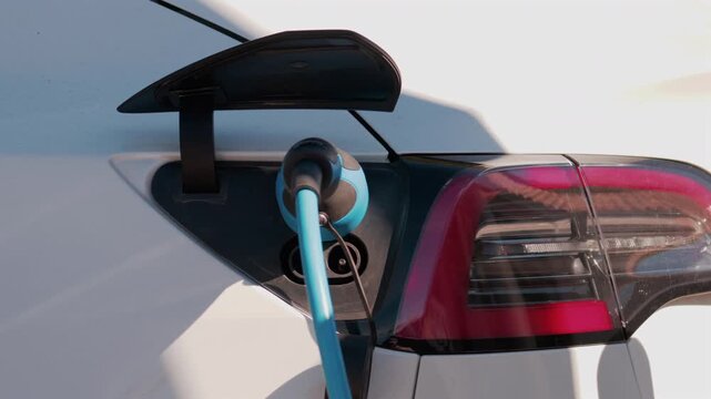 Close up of an electric car plugged into a blue charging cable in daylight