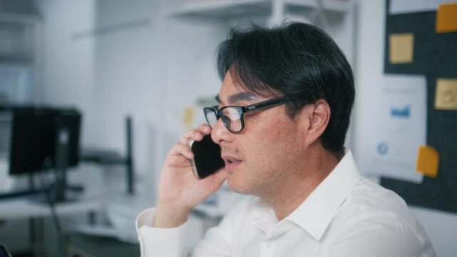 Professional Businessman working on computer and talking on mobile phone sit at desk in office. Mature Asian Marketing sales manager phone call with client, negotiating speaking on cell phone.