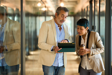 Business colleagues collaborating on digital tablet in office hallway - legal, insurance and financial advisory