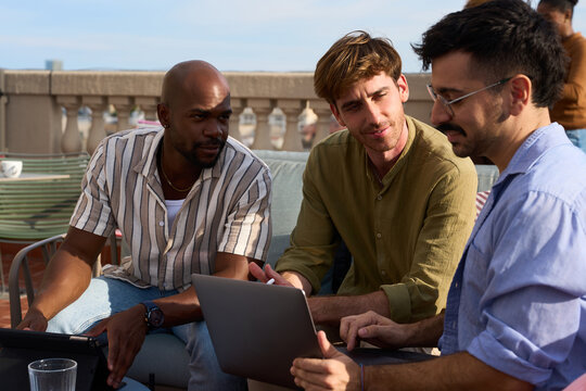 Diverse men collaborating outdoor with laptop on a rooftop