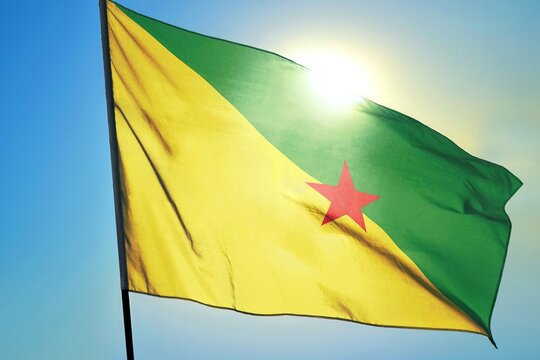 French Guiana flag waving in sunlight close-up – French overseas department banner green and yellow diagonal field with red star patriotic South America region symbol background blue sky sunny day - Powered by Adobe
