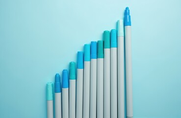 Group of blue and teal markers arranged in ascending order on light blue surface. Pens vary in size creating stair step effect. This simple composition suggests growth progress or creative start.