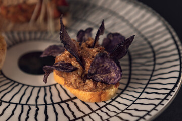 Gourmet toast with meat spread and purple chips on designer plate