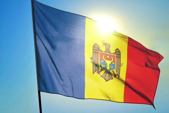 Moldova national flag waving in sunlight close-up &ndash; Moldovan tricolor blue yellow red banner with coat of arms eagle holding cross olive branch scepter patriotic background blue sky bright sunny day
