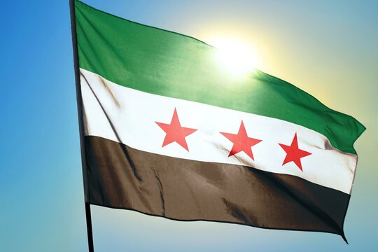 Syria flag waving in sunlight close-up &ndash; Syrian tricolor green white black banner with three red stars patriotic symbol of freedom revolution background blue sky bright sunny day
