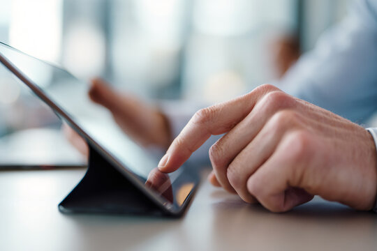 A close-up of a person's hand touching a digital tablet screen. Man using a mobile device for work or browsing online. Business and technology concept - Powered by Adobe