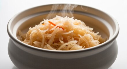 A bowl of steaming, shredded cabbage-like dish, light colored with slight orange accent, set against white