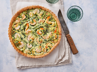 A delicious shrimp and spinach quiche sits on a light tablecloth, showcasing a golden crust and vibrant filling. Clear glass cups surround the dish, inviting enjoyment