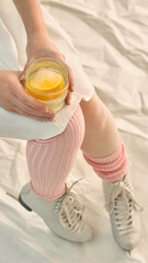Close-up woman holding glass with lemon drink wearing ice skates. Concept of generational culture and digital content, seasonal style, apres-sport rituals, and visual storytelling.