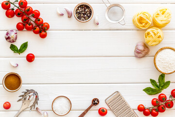 Frame of ingredients for cooking Italian pasta - uncooked fettuccine with tomatoes and basil leaves - on a white wooden background, top view