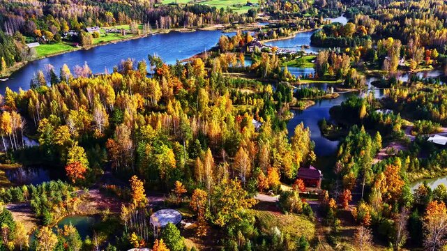 Aerial of autumn forest surrounding calm meandering lake water with colorful reflections and trees, community homes connected between islands
