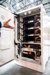 Hand gestures at an open high-tech energy storage system cabinet, revealing rows of advanced power modules and intricate wiring. Modern battery technology for industrial applications and renewable ene