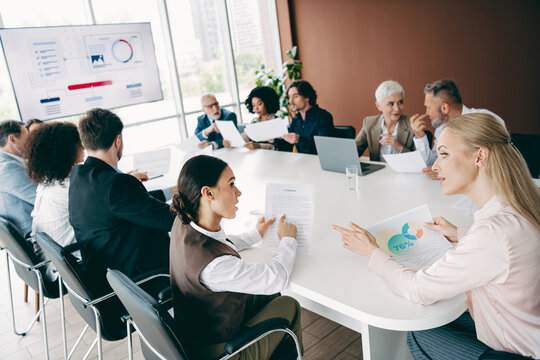 Diverse team collaborates in office, discussing ideas and sharing insights at a group meeting involving reports and presentations - Powered by Adobe