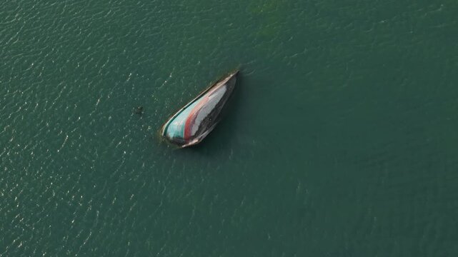 Drone backwards reveal from top-down view of capsized boat expanding to wide angle showing tropical coastline and emerald waters