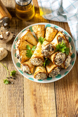 Crispy lavash rolls with mushroom filling, cheese and herbs on a rustic wooden table. Copy space.