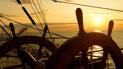 ship's wheel of an old sailing ship at sunset