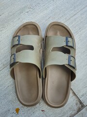 Top-down view of casual, waterproof olive green rubber slide sandals with faux dark blue buckles, resting on a light grey tiled floor. Focus on comfortable, practical footwear for e-commerce or summer