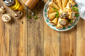 Crispy lavash rolls with mushroom filling, cheese and herbs on a rustic wooden table. Top view.