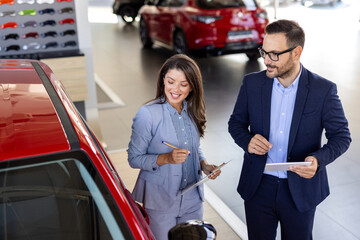 Confident sales team in dealership, two beautiful consultants or managers in black full suit with...