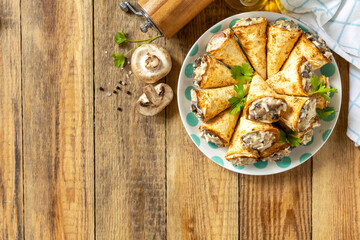Crispy lavash rolls with mushroom filling, cheese and herbs on a rustic wooden table. Top view.