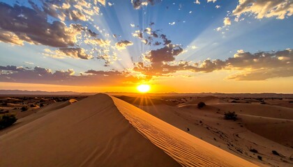 Golden sun bursts above the desert horizon, casting long rays through a partly cloudy, blue sky over sandy dunes