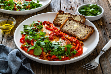 Shakshuka - fried eggs with red bell pepper and tomatoes  on wooden table