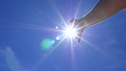 Person's hand reaching towards the bright sun against a clear blue sky, creating a beautiful lens flare effect. The spiritual concept of hope, freedom, and connecting with nature - Powered by Adobe