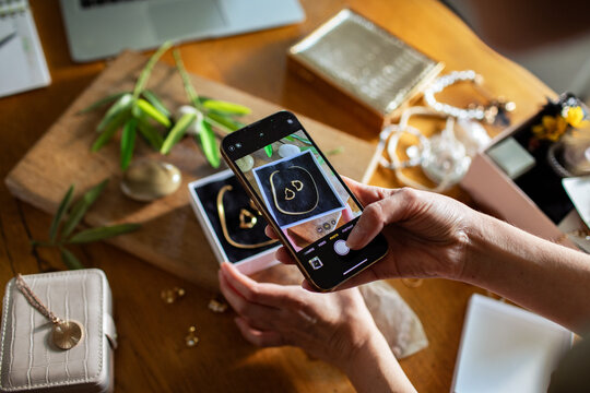 Young woman taking a photo of handmade jewelry with her phone before selling it online