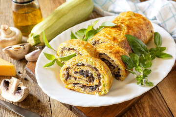Zucchini roll with mushroom filling and herbs served on a white plate on a rustic table.