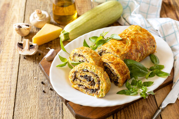 Zucchini roll with mushroom filling and herbs served on a white plate on a rustic table.