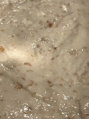 Thick, sticky bread dough with visible grains being mixed in a glass bowl