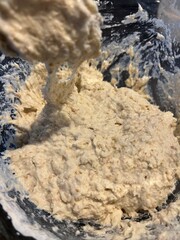 Thick, sticky bread dough with visible grains being mixed in a glass bowl using a metal spoon