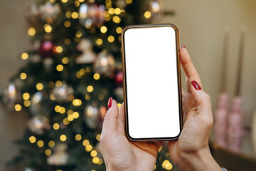 Mockup woman's hand holding using smart phone with white blank screen at Christmas light background, mobile app design and advertising, online marketing