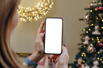Mockup woman's hand holding using smart phone with white blank screen at Christmas light background, mobile app design and advertising, online marketing