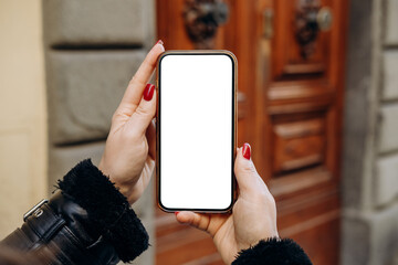 Mockup woman's hand holding using smart phone, Hands are holding a smartphone featuring a blank screen, positioned in front of a wooden door, real estate rent, mobile app design and advertising