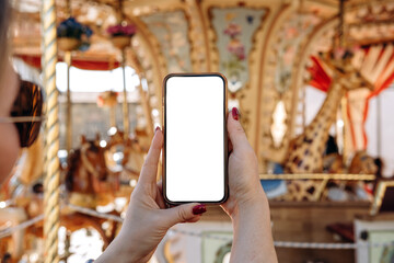 Smartphone mock up held by hands with blank screen, set against a vibrant carousel background, ideal for design and marketing purposes