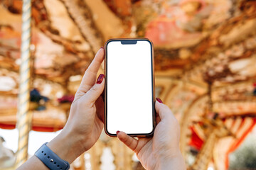 Smartphone mock up held by hands with blank screen, set against a vibrant carousel background, ideal for design and marketing purposes