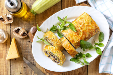 Zucchini roll with mushroom filling and herbs served on a white plate on a rustic table. Top view.