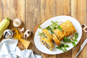 Zucchini roll with mushroom filling and herbs served on a white plate on a rustic table. Top view.