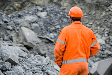 A worker with safety attire in orange oversees a quarry, ensuring compliance and safety in mining, construction and the environment. This photo highlights work ethic and oversight.