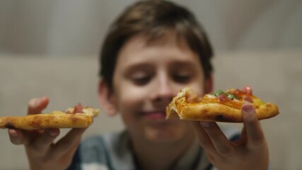 A smiling Caucasian boy of 11 years old looks at slices of pizza holding them in his hands in anticipation of a tasty snack. The child eats pizza with pleasure.