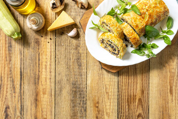 Zucchini roll with mushroom filling and herbs served on a white plate on a rustic table. Top view.