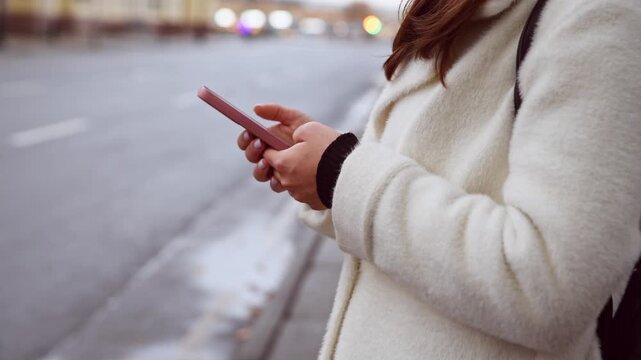 Woman ordering taxi via phone app on city street at dusk