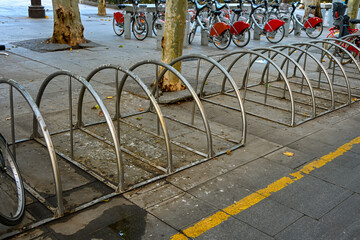 Empty metal bike racks in the foreground with shared bicycles parked in the background on a city street in Seville