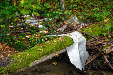 Plastic junk and debris litter a lush stream bank, an eyesore on nature. Water flow brought this environmental mess ashore, highlighting pollution's impact