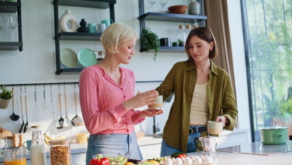 Two girls clinking coffee cups at cozy kitchen closeup. Lgbt pair breakfasting