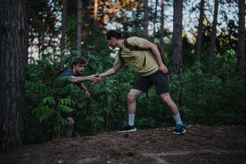 Two men in a wooded setting assist one another along a forest trail. One reaches out to help the other, highlighting teamwork, resilience, and outdoor exploration.